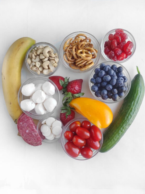 Ingredients in small bowls and fresh produce arranged on a white surface for a patriotic charcuterie board.