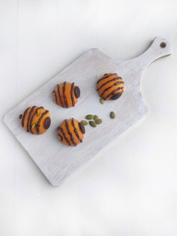 Chocolate-dipped apricots styled as bees on a small white board