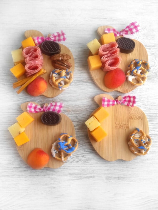 Four wooden apple-shaped boards partially assembled with charcuterie items.