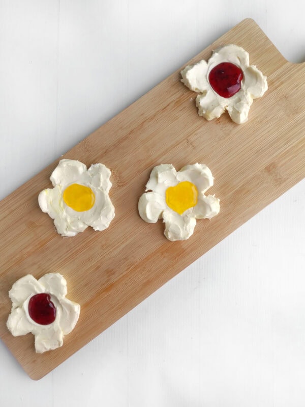 Whipped cream flowers with yellow and red jelly centers on a cutting board