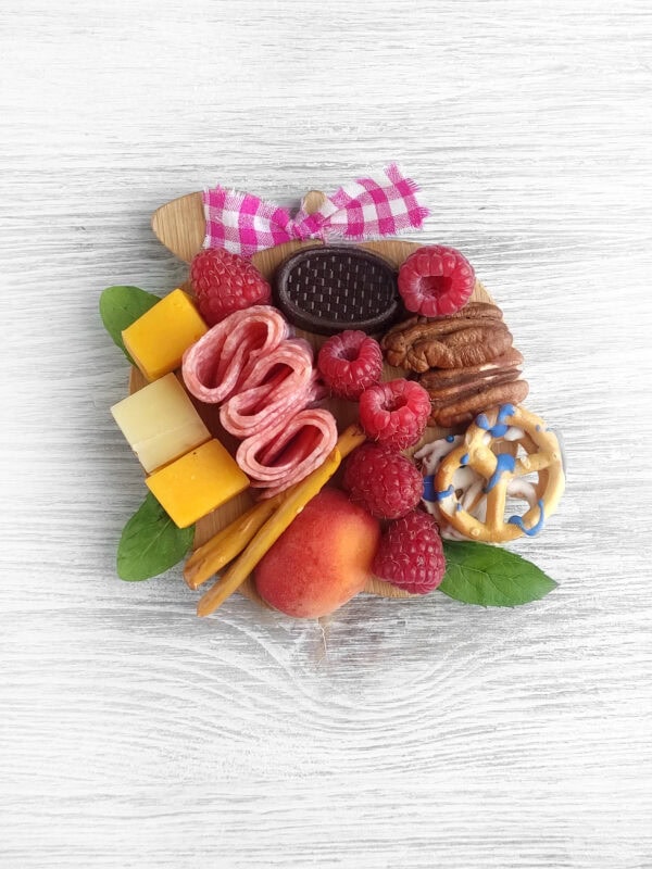 Close-up of a fully assembled mini charcuterie board with fruit, cheese, meat, and snacks.