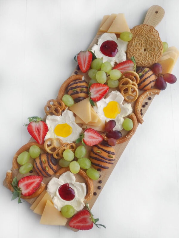 Colorful charcuterie board with fruit, cheese, pretzels, and floral elements