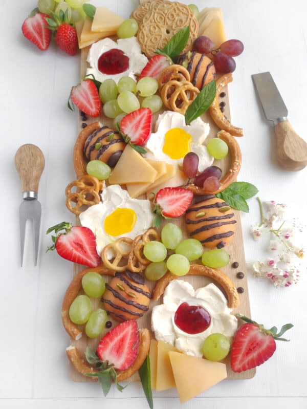 Top view of summer flower charcuterie board with grapes, strawberries, cheese, and cream flowers