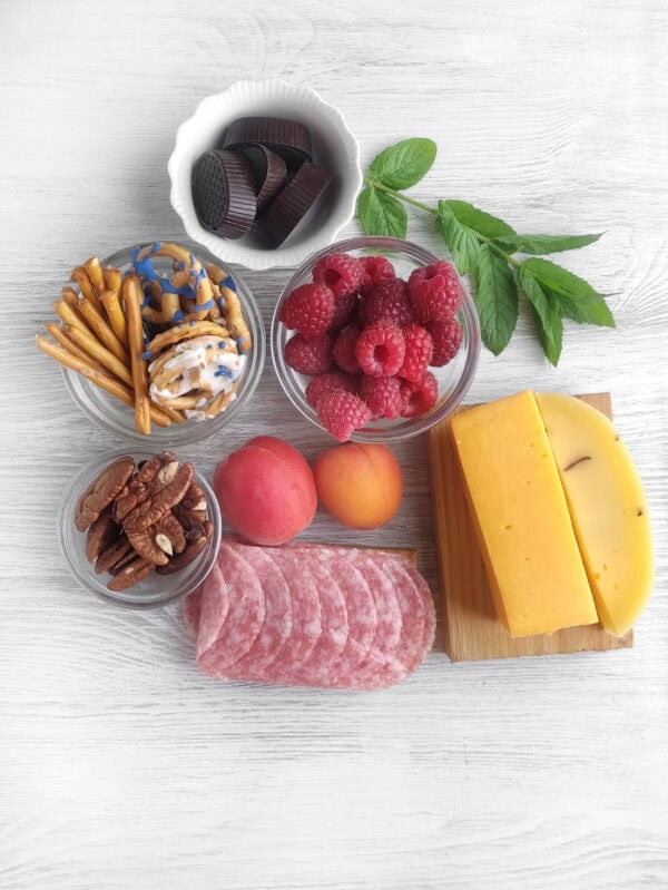 Ingredients for mini charcuterie board including cheese, fruit, meats, and snacks.