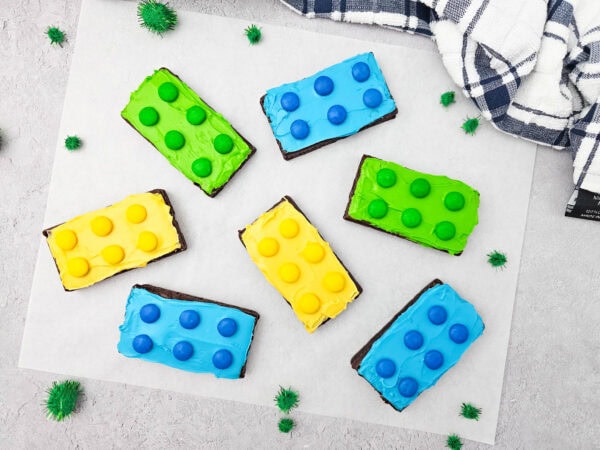Assorted decorated LEGO brownies in blue, green, and yellow with candy dots on parchment paper