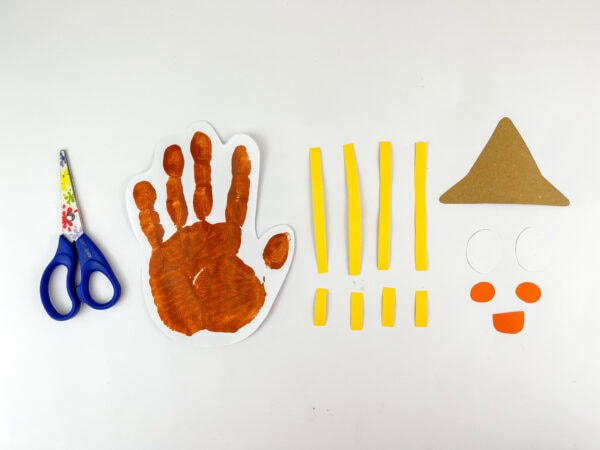 Cut-out handprint and scarecrow parts laid out with scissors
