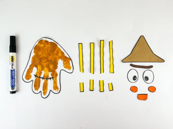 Painted handprint and scarecrow face pieces with black marker beside them