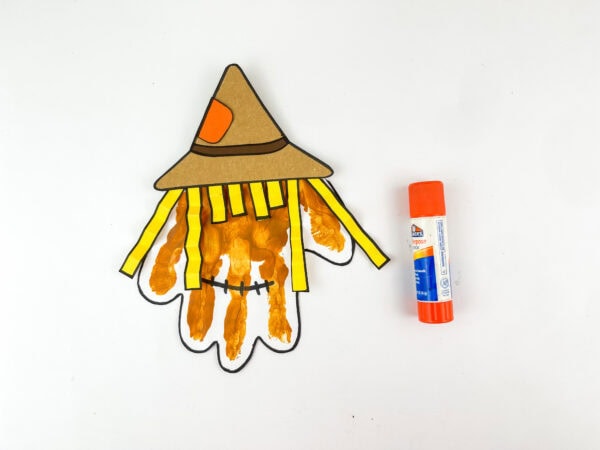 Partially assembled scarecrow with hat and hair beside glue stick