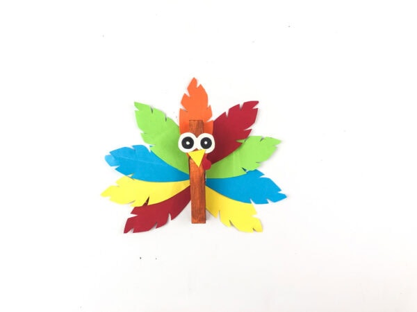Finished turkey clothespin craft with bright paper feathers.