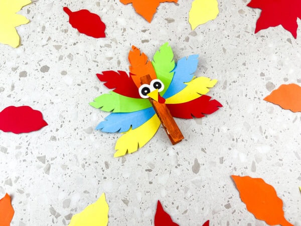 Turkey clothespin craft surrounded by paper leaves on a table