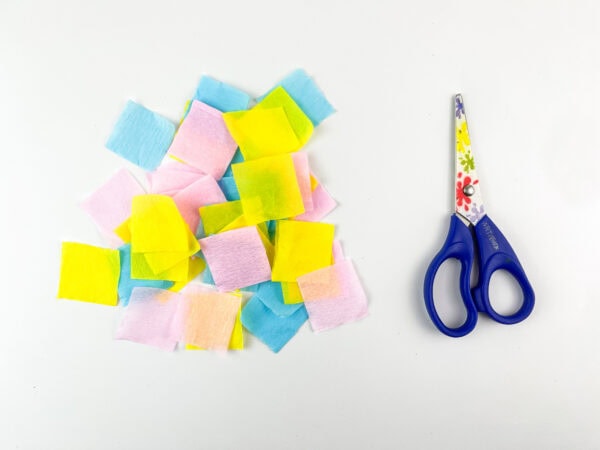 Pile of colorful tissue paper squares with scissors.