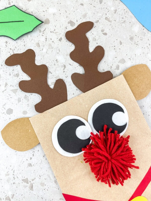 Close-up of reindeer paper bag craft with big eyes, red pom-pom nose, and antlers