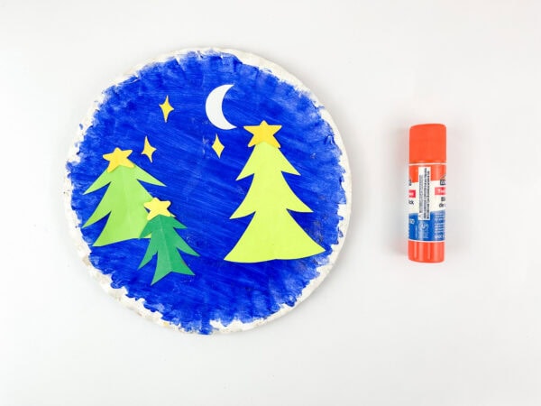 Blue paper plate with glued trees and stars