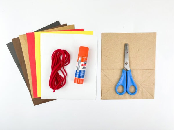 Craft supplies with colored paper, yarn, glue stick, scissors, and paper bag.