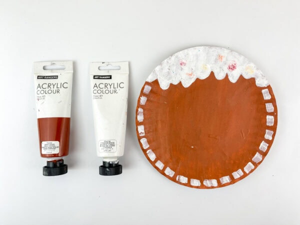 Painted brown paper plate with white icing details and paint tubes beside it