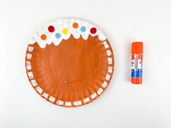 Brown paper plate with glued-on colorful candy dots and glue stick beside it
