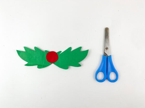 Green holly leaves and red berry cutouts with scissors
