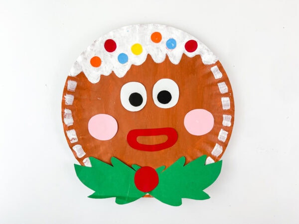 Finished gingerbread paper plate craft with colorful candy dots and holly bow
