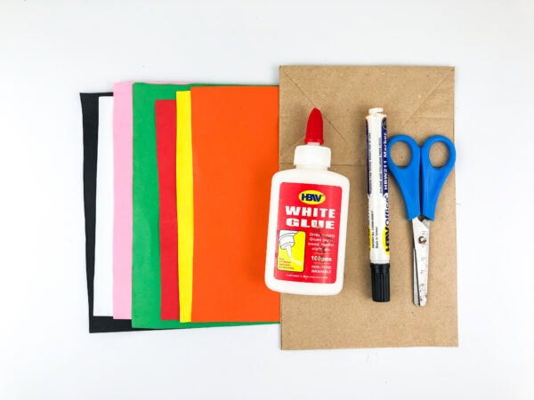 Craft supplies including paper sheets, glue, scissors, marker, and paper bag.