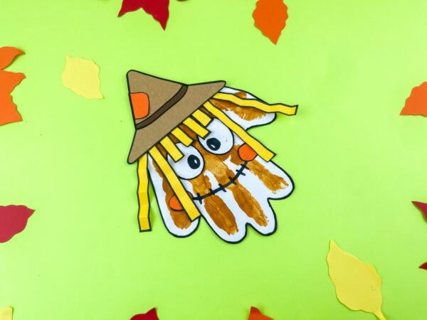 Scarecrow handprint craft surrounded by paper fall leaves