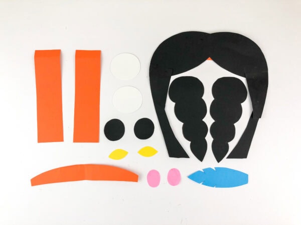 Cut-out craft pieces including hair, braids, eyes, feathers, and clothing.