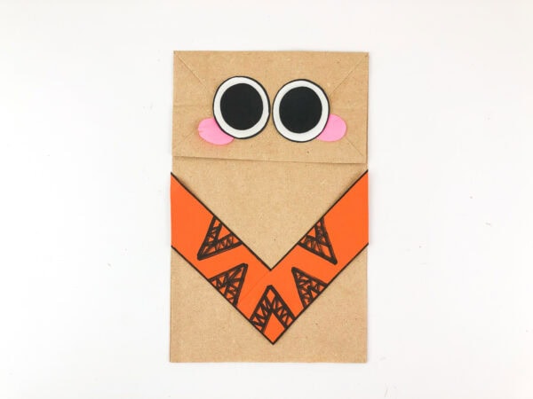 Paper bag puppet with eyes and cheeks attached above clothing.