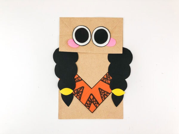 Paper bag puppet with eyes, cheeks, braids, and yellow hair ties.