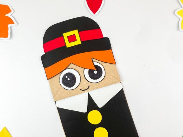 Pilgrim boy paper bag craft shown upright with colorful leaves around.