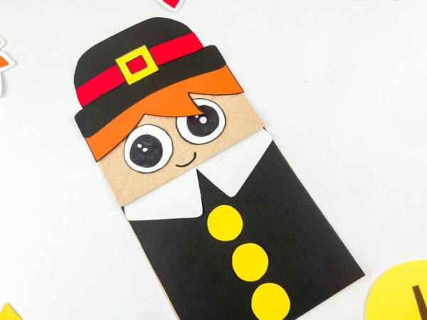 Pilgrim boy paper bag craft with big eyes and three yellow buttons on black outfit.