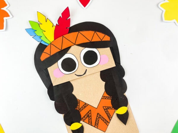 Close-up of finished paper bag girl craft with braids and feathers.