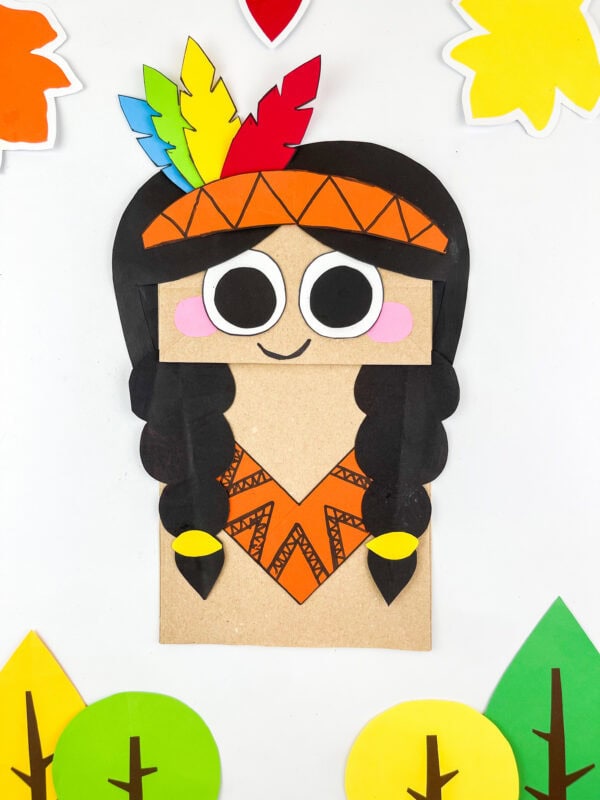 Paper bag craft girl with black braids, orange outfit, and colorful feather headband.