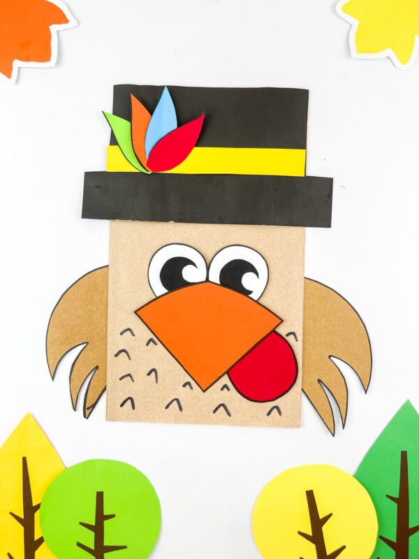 Pilgrim turkey paper bag craft surrounded by colorful paper trees.