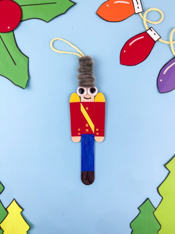 Nutcracker ornament on blue background with paper holly and Christmas lights.