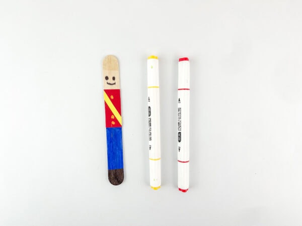 Popsicle stick with red jacket and yellow sash drawn.