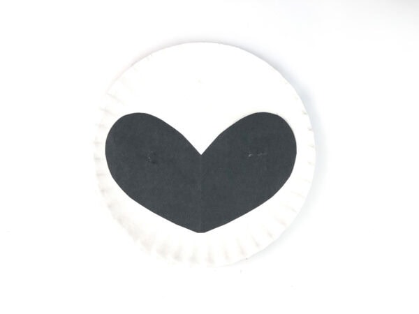 Black face mask shape glued onto a white paper plate.