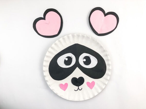 Paper plate panda face with two heart-shaped ears above it.