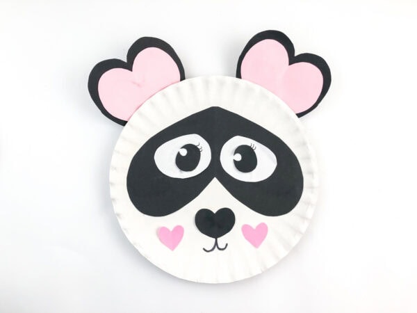 Paper plate panda craft with attached pink heart ears.