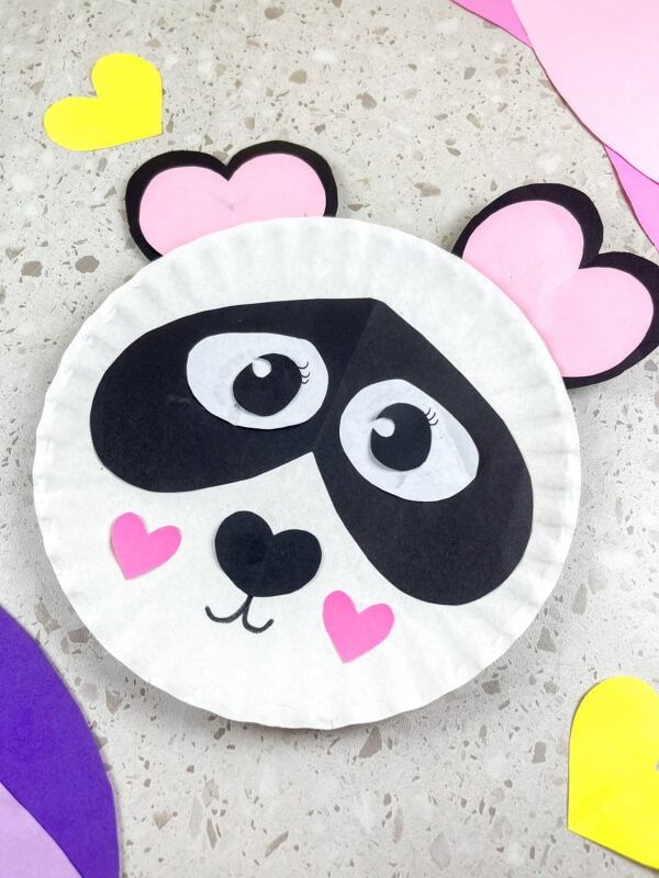 Finished panda paper plate craft surrounded by colorful paper hearts.
