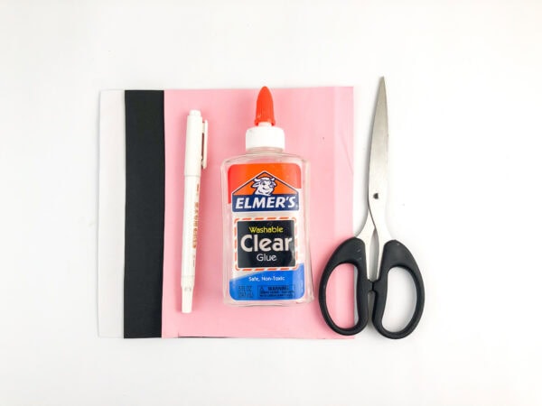 Pink and black paper, glue, scissors, and white pen arranged on a table.