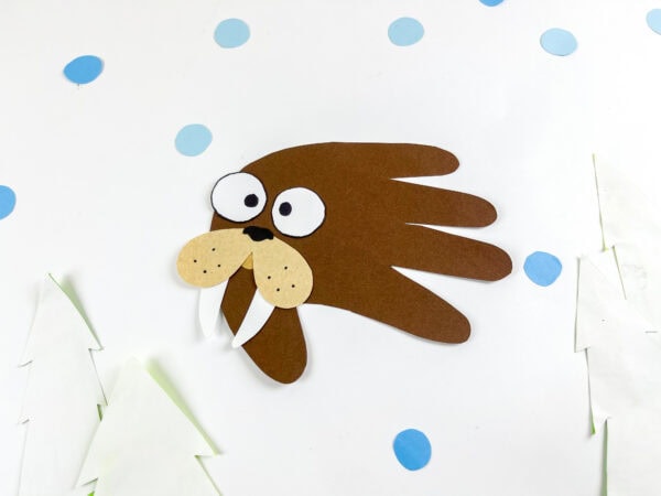 Walrus handprint craft placed on a snowy background with paper trees.