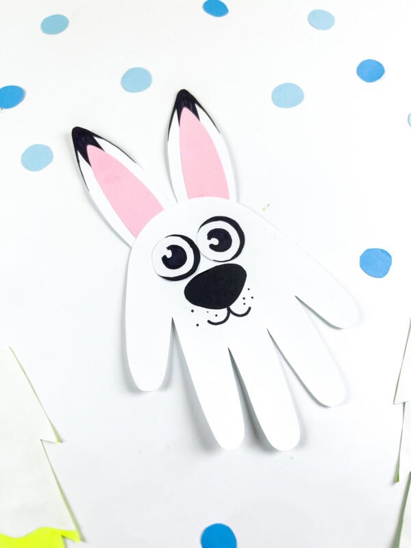Handprint arctic hare craft with pink ears and snowy blue dots in the background.