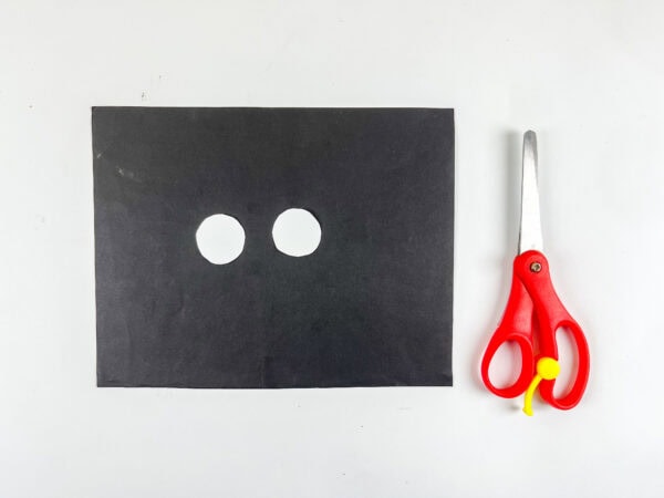 Black paper with two white circles cut out.