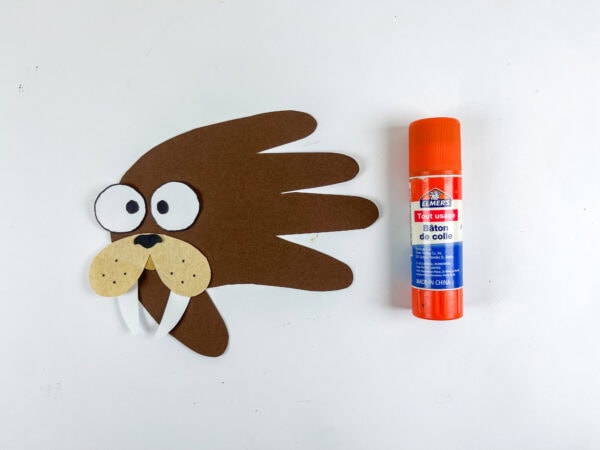 Walrus handprint craft with glued-on snout, eyes, and tusks next to a glue stick.