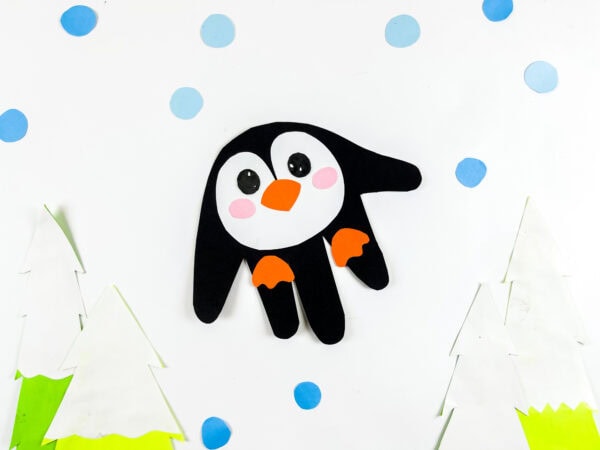 Penguin handprint craft displayed between paper trees and blue dots.