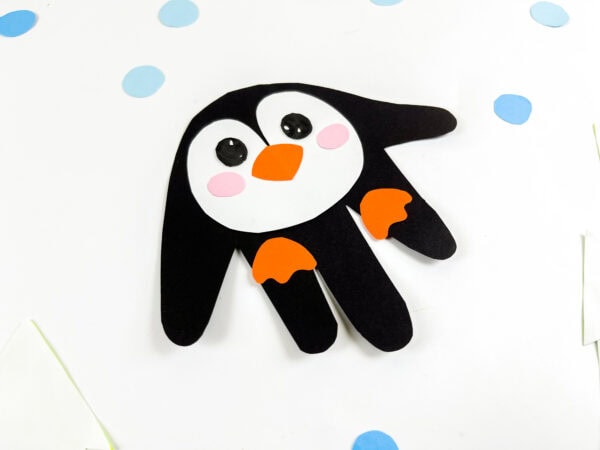 Penguin handprint craft placed on a snowy background with blue dots.