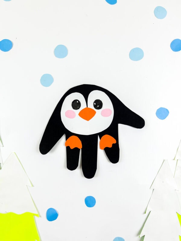 Finished penguin handprint craft on snowy background.
