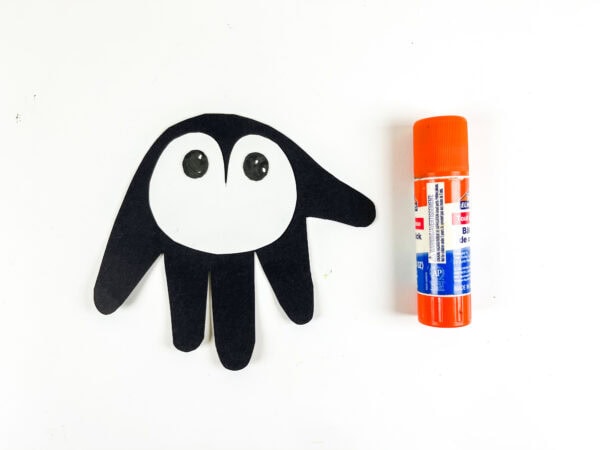 Penguin craft with eyes glued on and glue stick beside it.