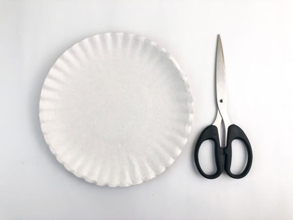 Plain paper plate and scissors on a white background.