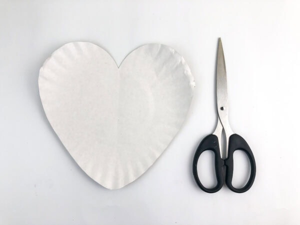 Paper plate cut into a heart shape beside scissors.