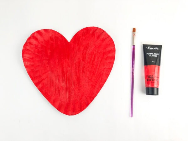 Heart-shaped paper plate painted red with brush and paint.